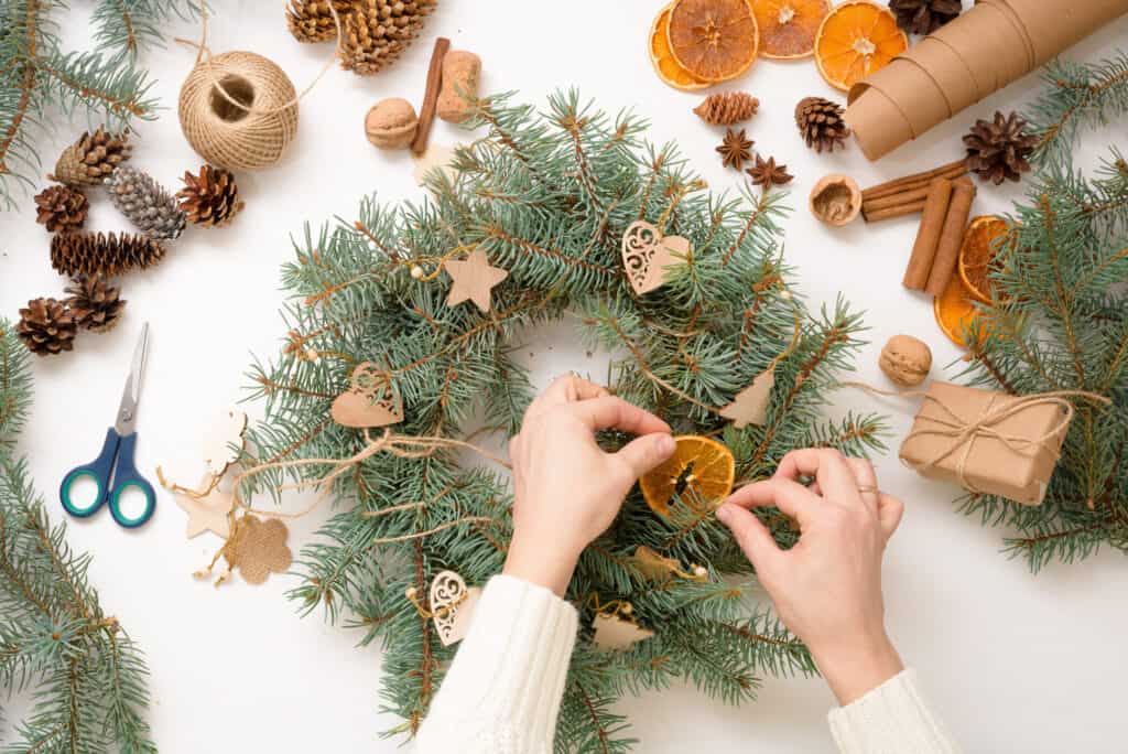 step-by-step process of making Christmas tree wreath at home from spruce branches, oranges and wooden eco-friendly toys in 2021. white background top view. concept of ecological Christmas, waste-free.