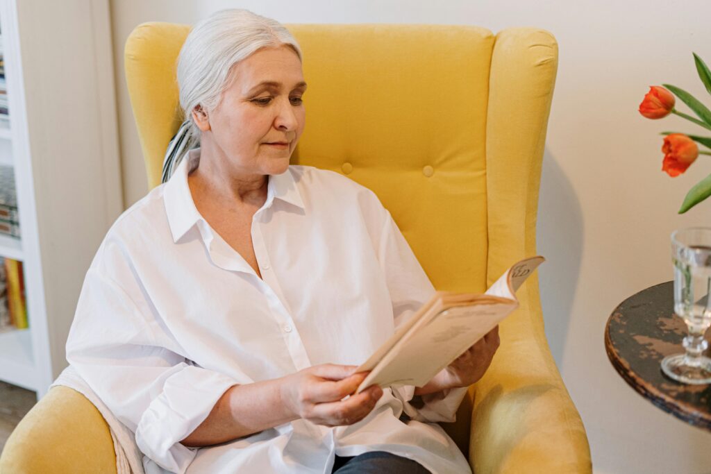 Older woman sitting in a yellow chair reading a book.