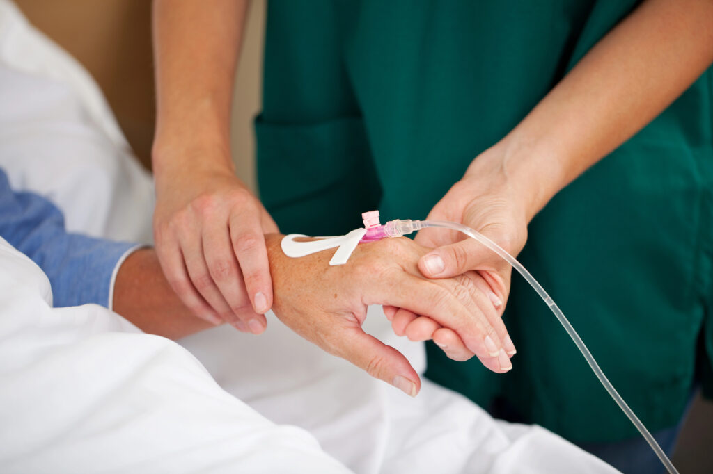 Person with an IV being attended to by a nurse in green scrubs.