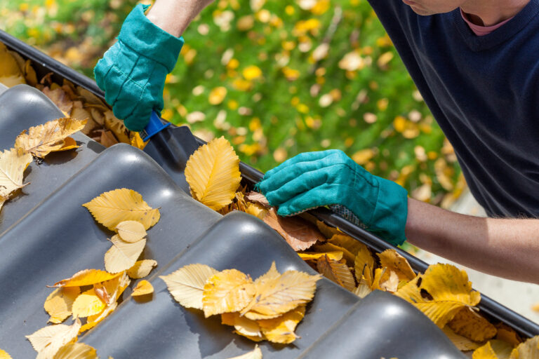Person wearing gloves cleaning out a gutter.
