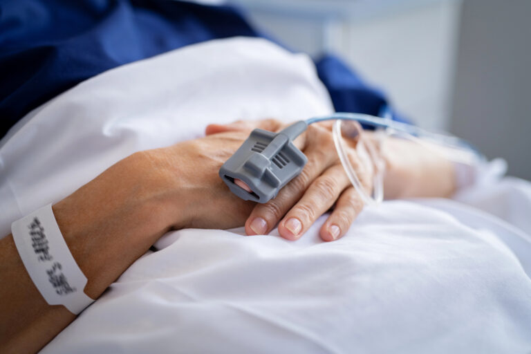 Woman laying in a hospital bed with a monitor on her hand.