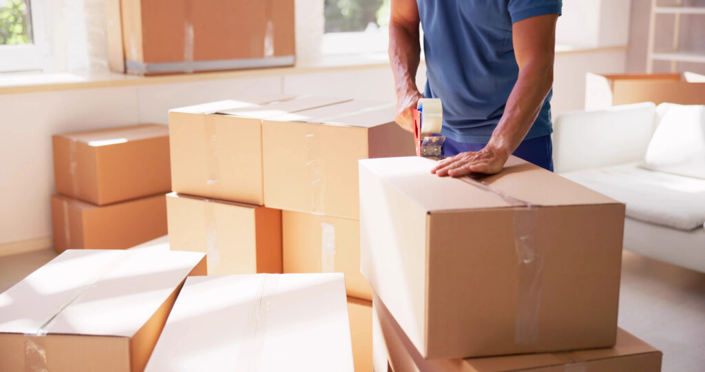 Man in a blue shirt taping up a moving box.