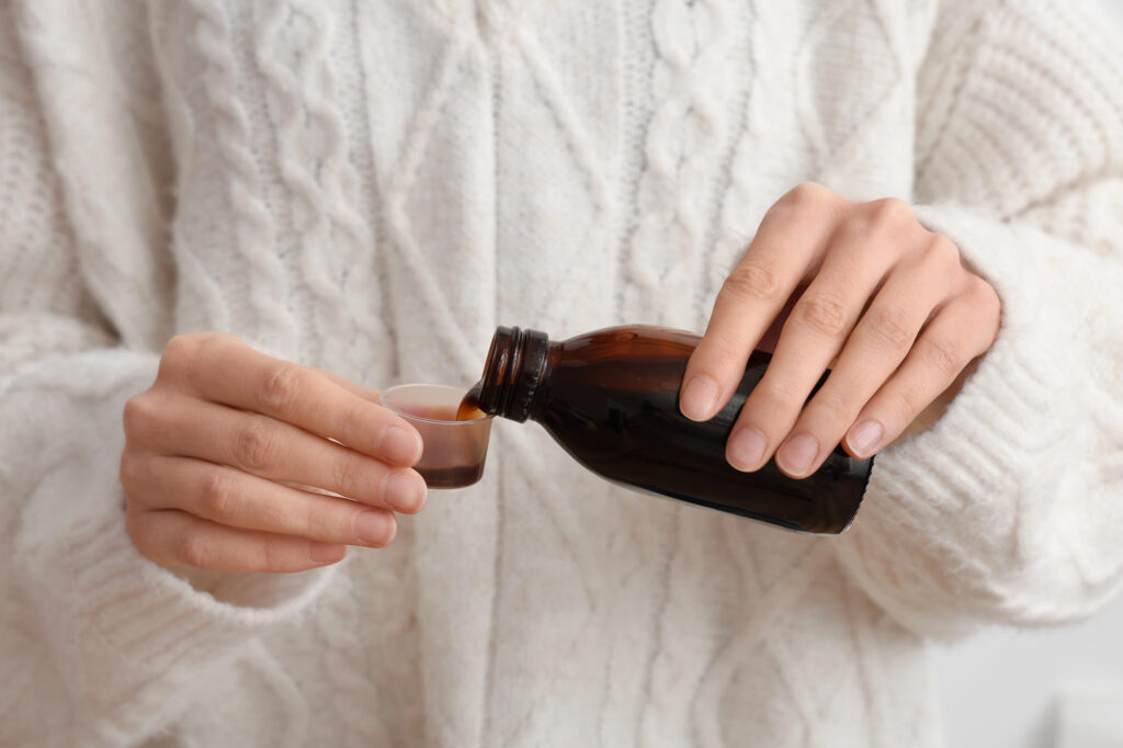 Woman in a white sweater pouring elderberry syrup in a medicine cup.
