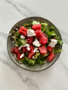 Watermelon and feta over salad in a bowl on a marble countertop.
