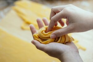Woman holding a handful of homemade fettuccine noodles next to a pasta maker.