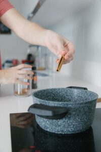 Woman putting a cinnamon stick into a pot on the stove.