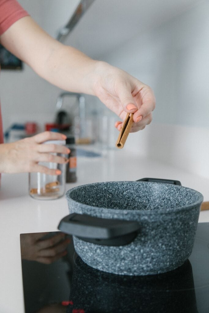 Woman putting a cinnamon stick into a pot on the stove.