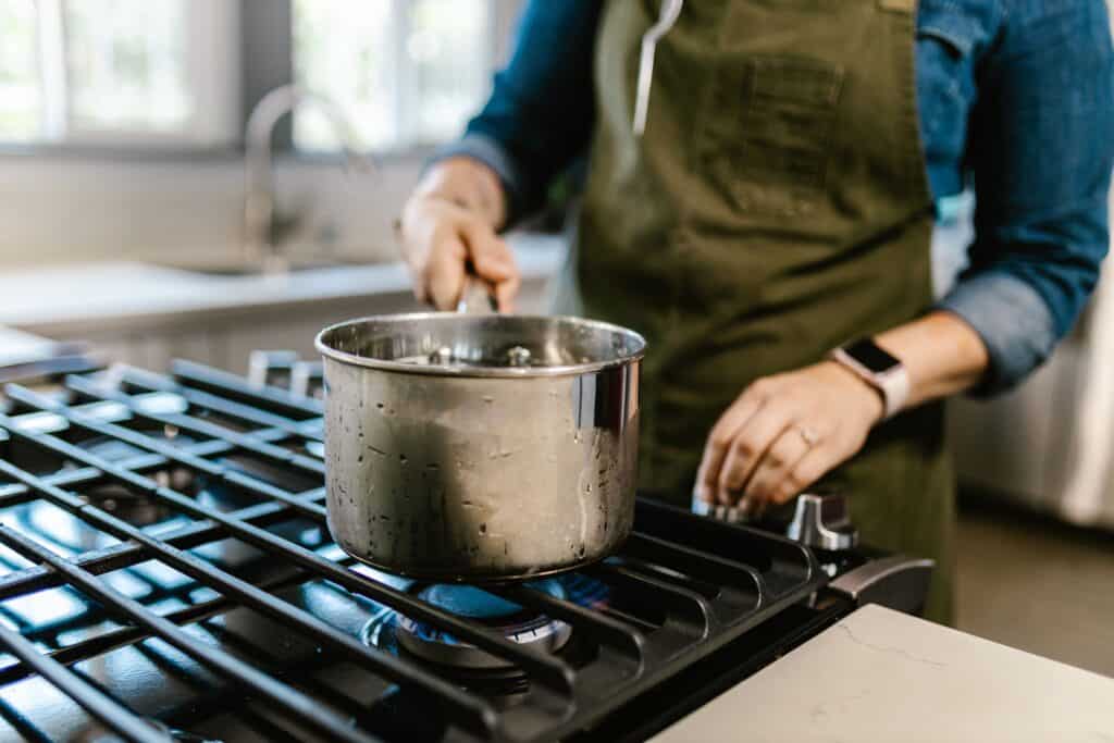 Woman cooking with a pot on a stove.